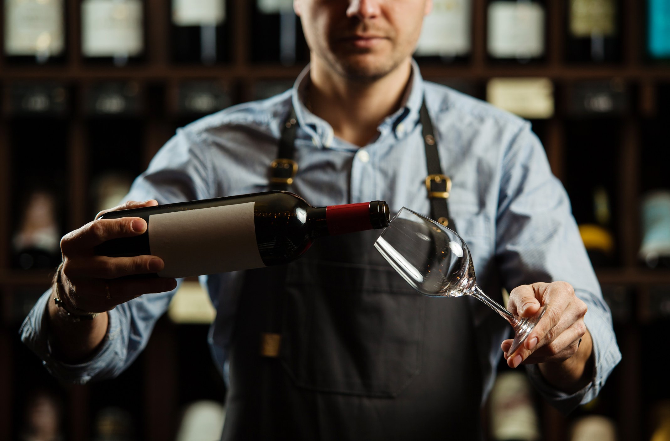 Male sommelier pouring red wine into long-stemmed wineglasses.